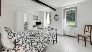 Un dormitorio con cama, una silla, un escritorio con televisor y una ventana.