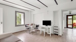 Una sala de estar moderna con sofá, mesa de comedor, sillas, televisor y un mueble blanco.