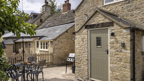 A stone cottage with a door, a barbecue, and a patio table with chairs. - Dog friendly cottage - The Roost (Coln St Aldwyns)