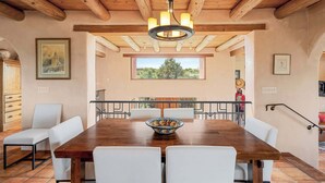 Un comedor con una mesa de madera, sillas blancas y una araña.