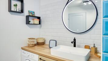 A modern bathroom with a washing machine, a sink with a mirror, and decorative baskets.