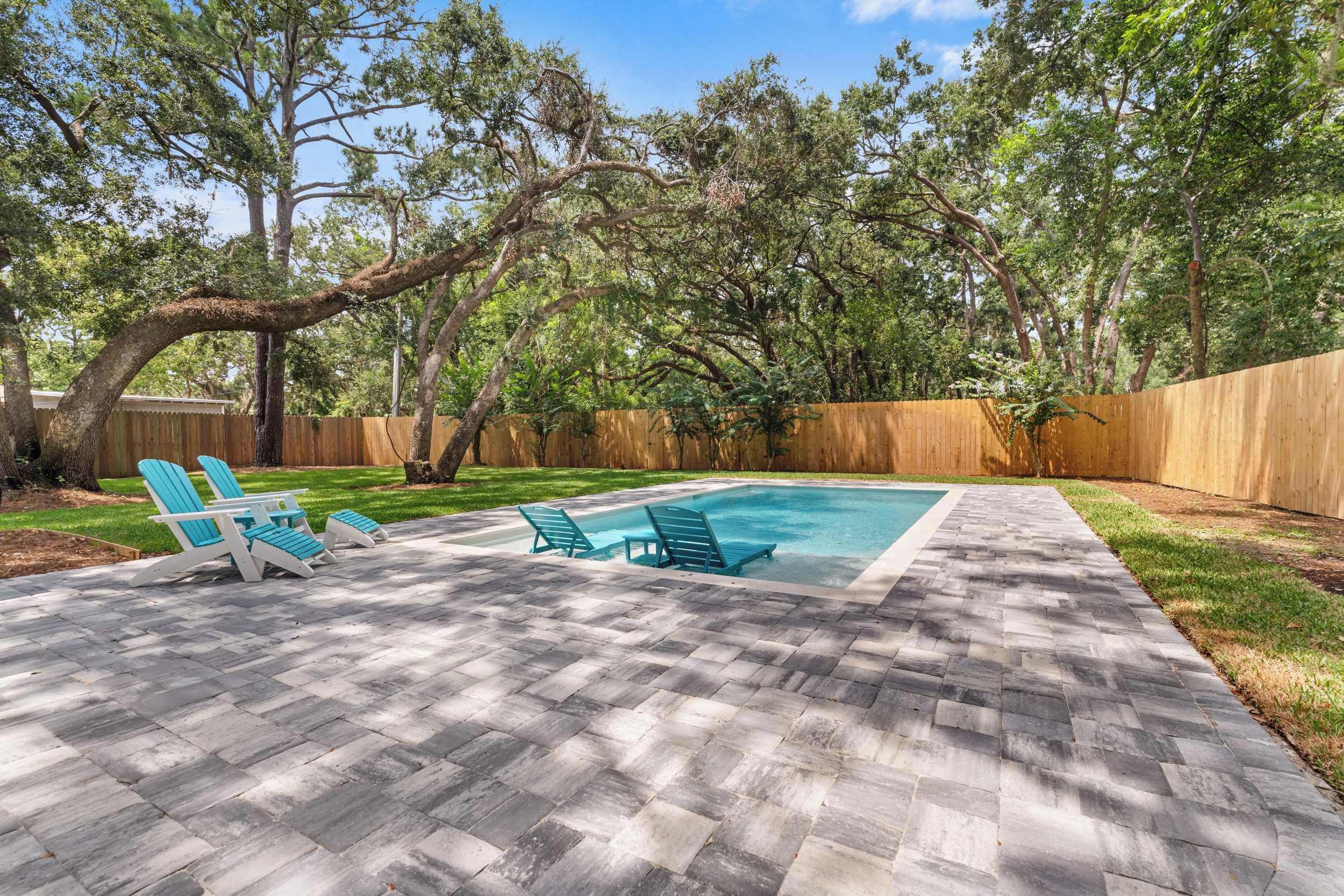 A backyard with a swimming pool, lounge chairs, and a wooden fence.