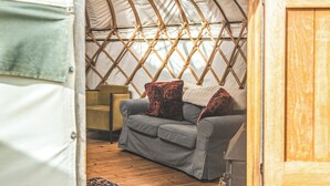 A cozy interior of a yurt with a grey sofa, a patterned rug, and a wooden door. - Willow Yurt - UKC6947 (Beaminster)