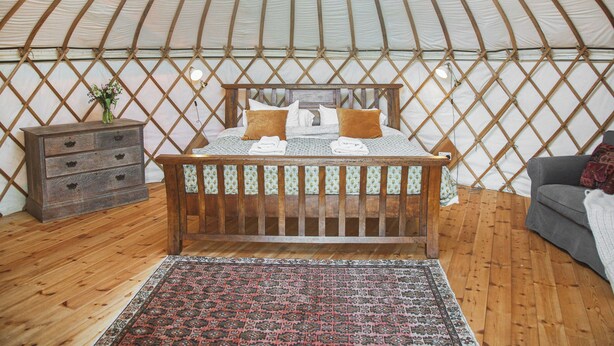 A cozy interior of a yurt with a wooden bed, a nightstand, and a patterned rug. - Willow Yurt - UKC6947 (Beaminster)