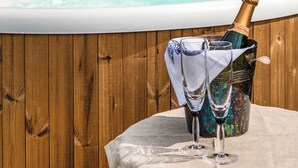 A wooden wall, a bathtub, a bottle of champagne, and two wine glasses on a table. - Willow Yurt - UKC6947 (Beaminster)