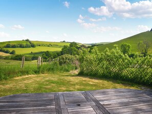 Una terraza de madera con vistas a colinas verdes ondulantes y un cielo despejado.