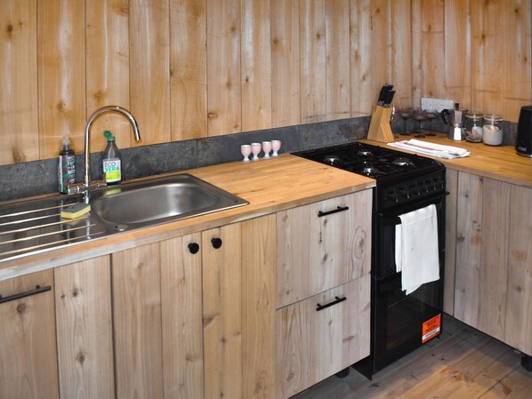 Una cocina con armarios de madera, un lavaplatos de acero inoxidable, una estufa y una encimera con diversos objetos.