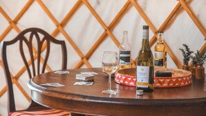 A round wooden table with a bottle of wine, a glass, and a decorative plate. - Skylark Yurt - UKC6946 (Beaminster)