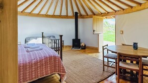 A yurt with a round skylight, a bed with a patterned blanket, a wooden table, and a chair. - Mistle Roundhouse - UKC6943 (Beaminster)