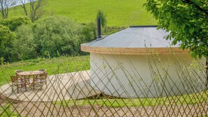 A small, single-story building with a flat roof, surrounded by a fence and a garden area with a table and chairs. - Mistle Roundhouse - UKC6943 (Beaminster)