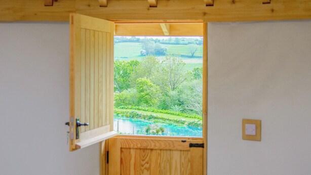 A room with a wooden door leading to a view of a green landscape. - Mistle Roundhouse - UKC6943 (Beaminster)