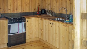 A kitchen with wooden cabinets, a stove, and a sink. - Mistle Roundhouse - UKC6943 (Beaminster)