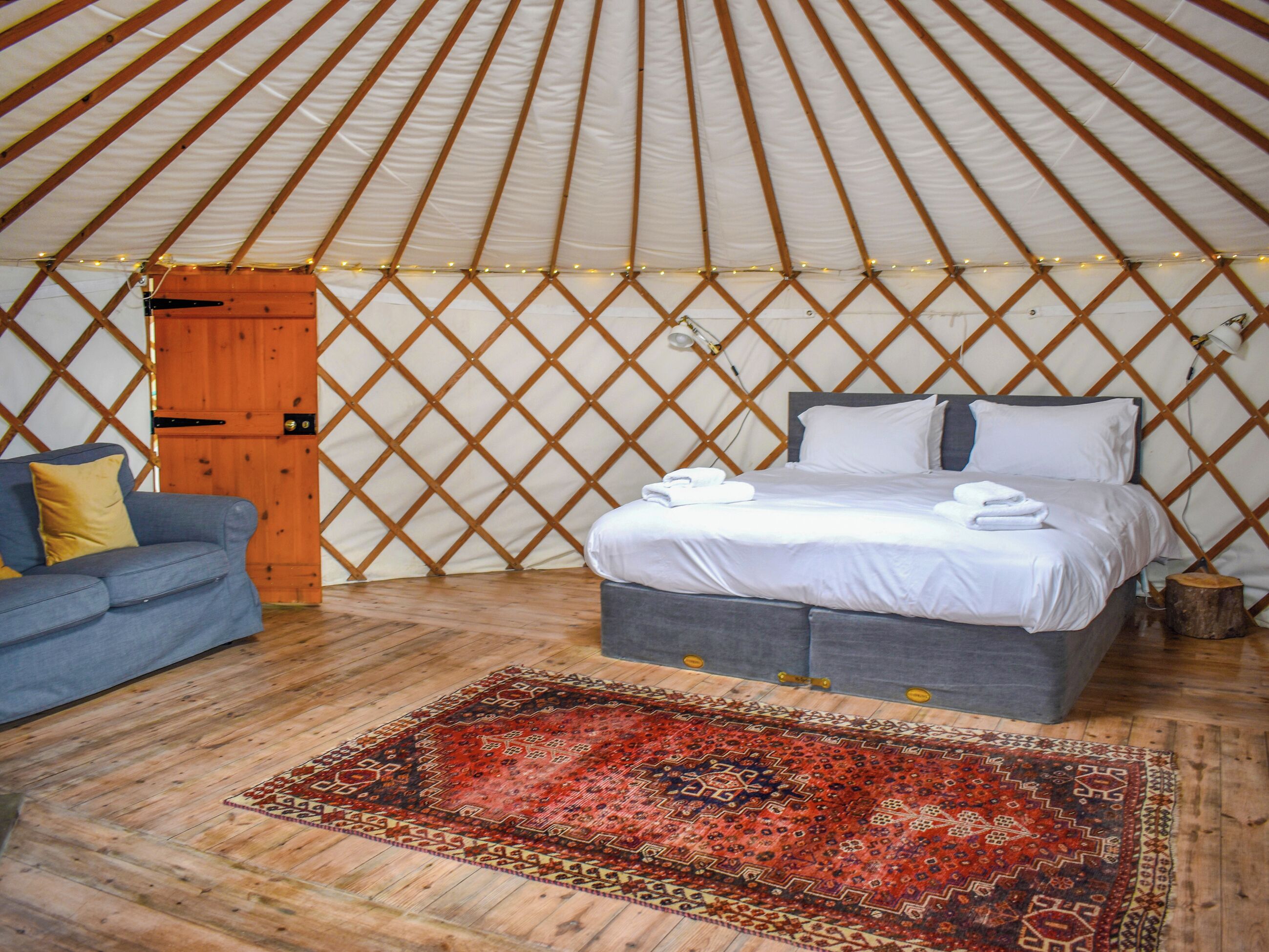 A cozy room with a bed, a sofa, a patterned rug, and a wooden door.
