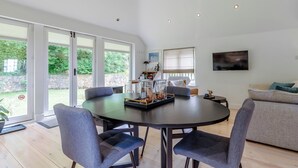 A modern living room with a dining area, large windows, and a flat-screen TV. - Fir Tree Apartment - UK49993 (Crowborough)