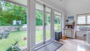A room with large sliding glass doors, a fireplace, a radiator, and a small table with books. - Fir Tree Apartment - UK49993 (Crowborough)
