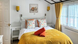 A bedroom with a bed, a bedside table, a lamp, a window with curtains, and a wall with a picture.