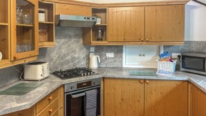 A compact kitchen with wooden cabinets, a gas stove, a microwave, and a toaster.