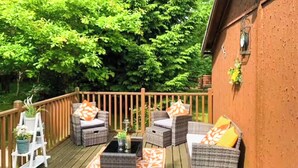 A wooden deck with wicker furniture and orange patterned rugs.