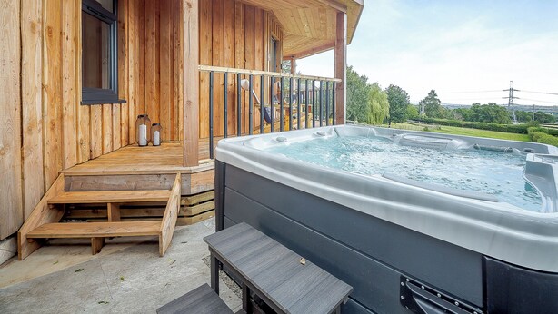 Une cabane en bois avec un jacuzzi, des marches en bois et un banc.