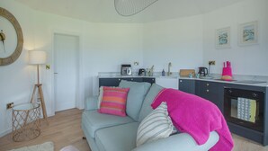 Un salon comprenant un canapé, une table basse, une lampe, ainsi qu’un coin cuisine avec un évier et une cuisinière.