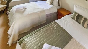 Habitación de hotel con dos camas, cada una con colcha verde y blanca. Entre las camas hay una mesita de noche de madera, y se ve una silla con un cojín estampado en la esquina.