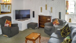 Ein Wohnzimmer mit Fernseher, zwei Sesseln, einem Sofa, einem Couchtisch aus Holz und einem Bücherregal.