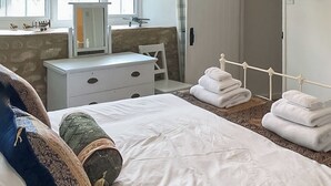 Een netjes opgemaakt bed met wit beddengoed, een klein nachtkastje en een stoel. Er liggen handdoeken op een stapel naast het bed.