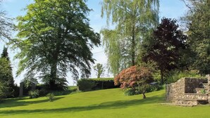 A well-maintained lawn with a stone structure, surrounded by various trees and greenery. - 2 bedroom accommodation in Membury (Membury)