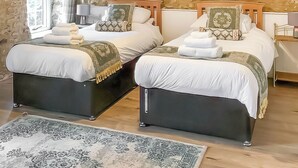 A double room with two beds, a stone wall, a window with curtains, and a patterned rug. - 2 bedroom accommodation in Membury (Membury)