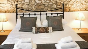 Un lit bien fait, avec du linge de lit blanc, deux oreillers ornés de motifs décoratifs et un coussin décoratif à motif floral. Deux lampes de chevet sont posées sur des tables de chevet en bois.