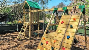 Una estructura de madera para escalar con una escalera y un tobogán, rodeada de árboles y una cerca.
