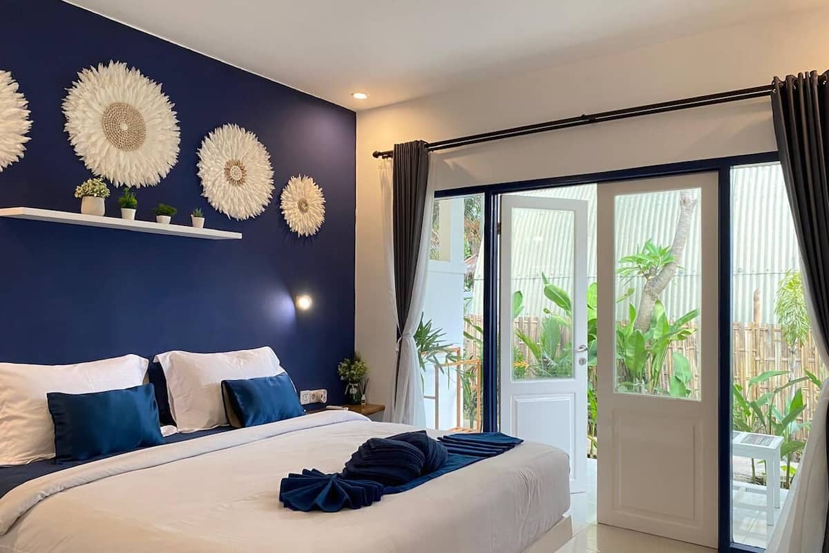 Een slaapkamer met een groot bed, een donkerblauwe accentmuur en uitzicht op een tuin door een schuifdeur.