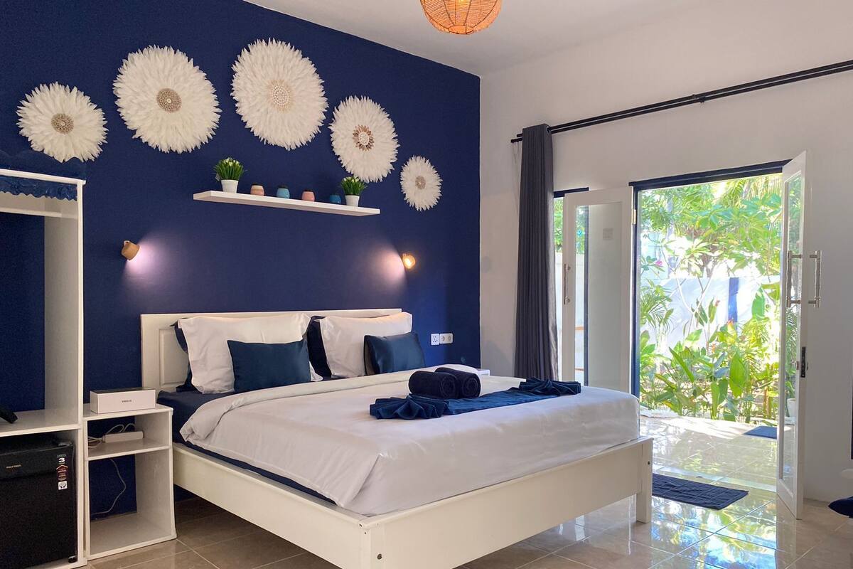 Een moderne slaapkamer met een wit bed, blauwe wanden en decoratieve wandkunst.