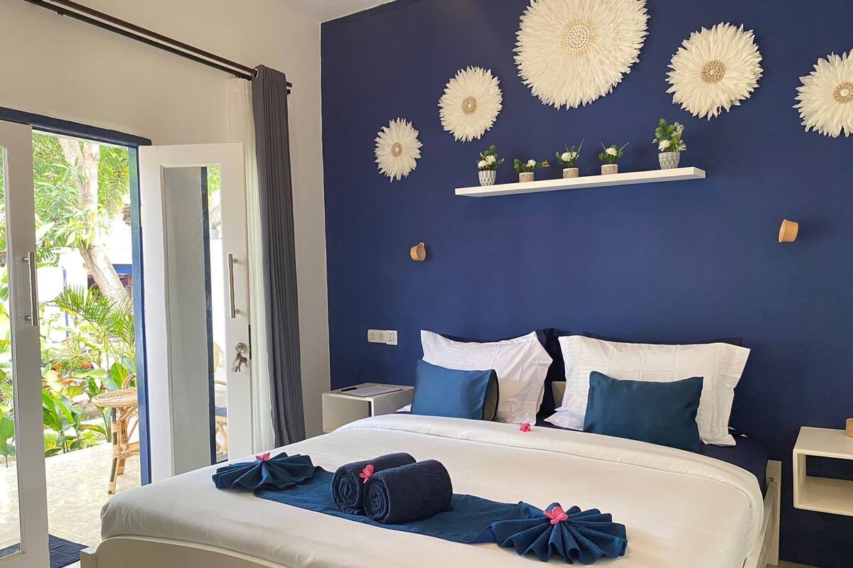 Een hotelkamer met een bed, nachtkastje, een plank met decoratieve objecten en uitzicht op de omgeving.