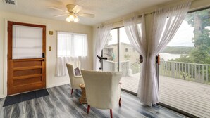 A room with a wooden door, a ceiling fan, a window with white curtains, and a view of a deck and lake.