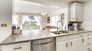 A modern kitchen with white cabinetry, stainless steel appliances, and a large window with curtains.