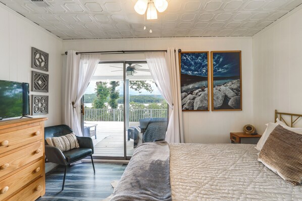 A bedroom with a bed, a dresser, a chair, and a view of a balcony with a railing. - Norfork Lake Views: Home w/ Deck in Henderson (Henderson)