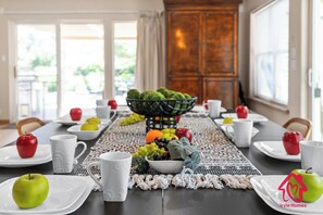 Une table à manger dressée avec des assiettes, des pommes et un panier de fruits.