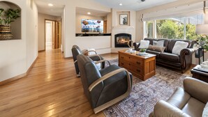 A spacious living room with a fireplace, leather sofas, a coffee table, and a television mounted on the wall. - The Rose Garden Estate with Swim Spa - an Irvie Home (Albuquerque)
