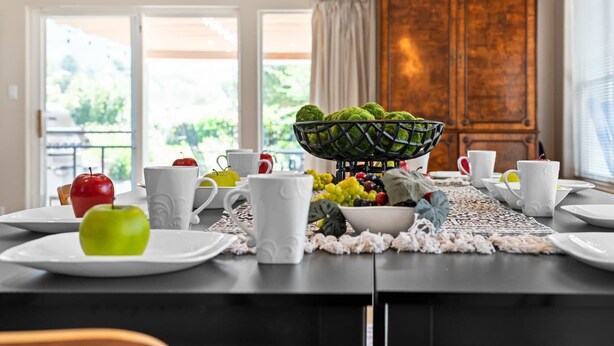 A dining table set with plates, cups, and a fruit bowl. - The Rose Garden Estate with Swim Spa - an Irvie Home (Albuquerque)