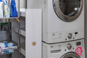Zona de lavandería con lavadora, botellas de detergente y una cesta con la etiqueta “THE GIANT BAG CLIP ”.