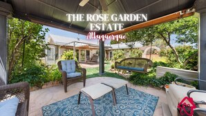 A covered patio area with wicker furniture, a swing, and a view of a house in Albuquerque. - The Rose Garden Estate with Swim Spa - an Irvie Home (Albuquerque)