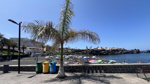 A beach with umbrellas, a palm tree, and a stone wall.