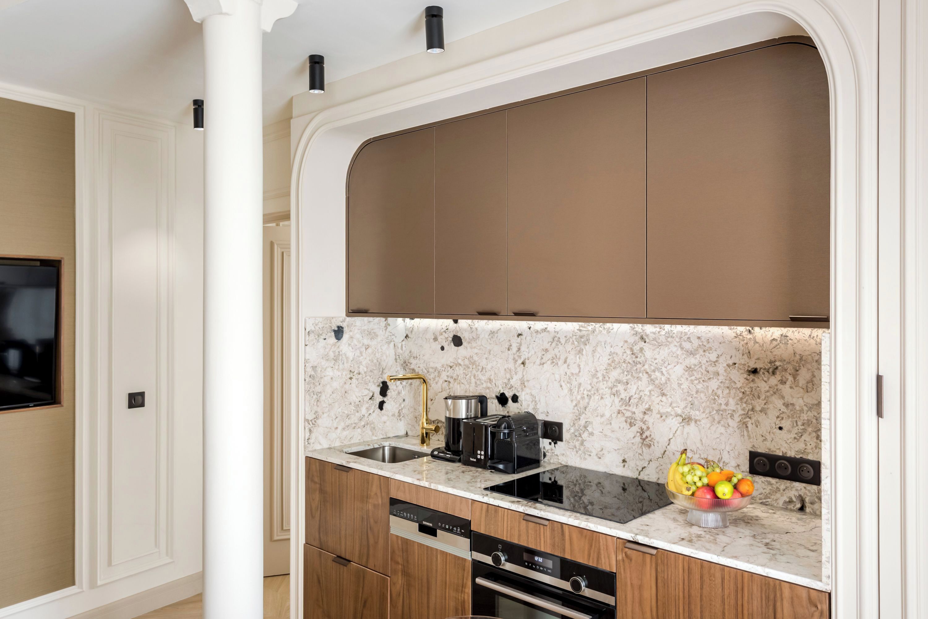 A modern kitchen with a marble countertop, built-in oven, and a fruit bowl.