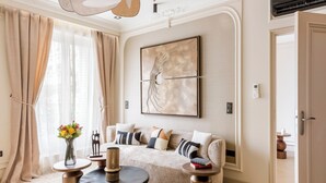 En moderne stue med en beige sofa, dekorative puder, et rundt sofabord og et stort abstrakt maleri på væggen.