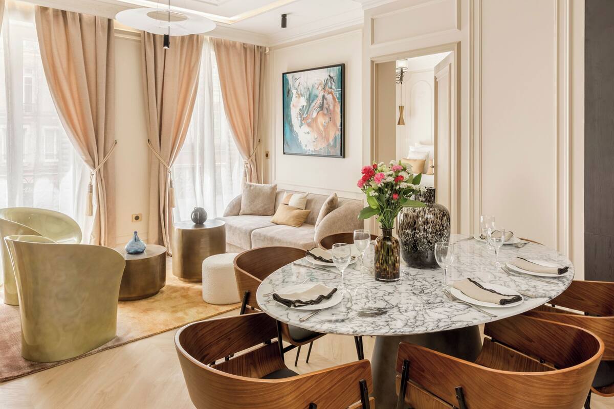 A dining area with a round marble table, wooden chairs, and a vase of flowers.