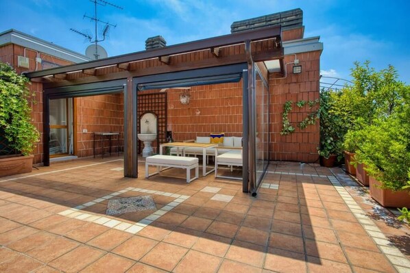 An outdoor patio with a pergola, seating area, and potted plants.