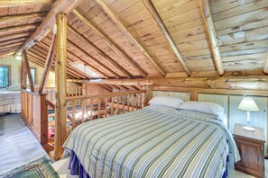 Um quarto aconchegante com teto de madeira, cama com roupa de cama listrada, mesa de cabeceira com abajur e vista para uma varanda.