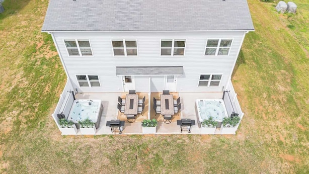 A two-story building with a patio area featuring outdoor seating and two hot tubs.