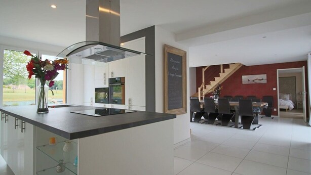 Cocina moderna con una isla central, un área de comedor con una mesa grande y una escalera que lleva a otro nivel.
